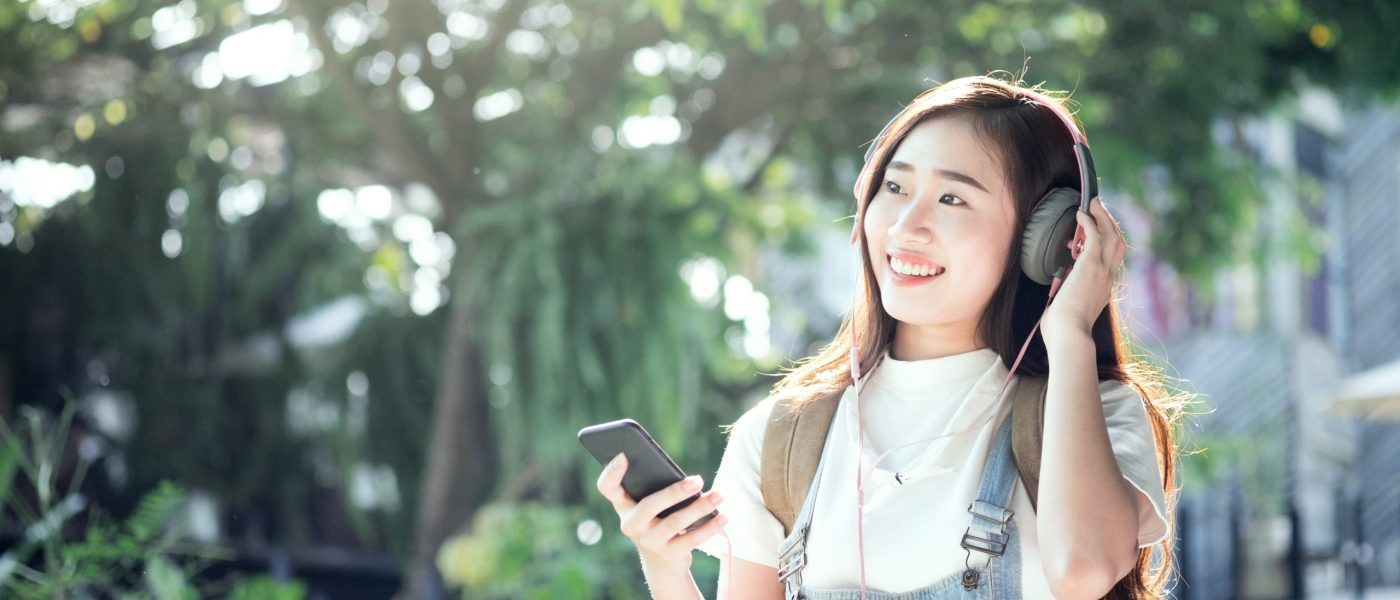 Young traveler hipster wear headphone listening to music through smartphone standing outdoors on nature background.
